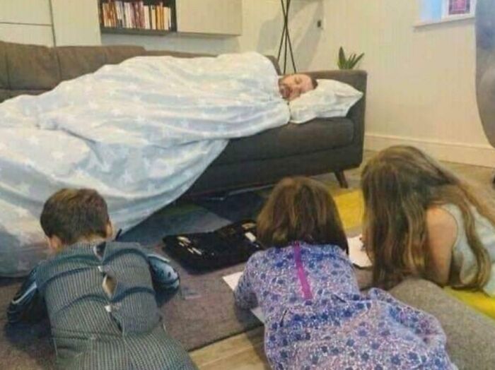 Dad sleeping covered with a blanket on a couch while kids work on homework nearby, showcasing hilarious dad moments.