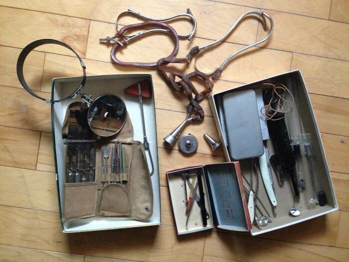 Vintage medical tools including a head mirror, stethoscope, scalpels, and syringes laid out on a wooden floor.