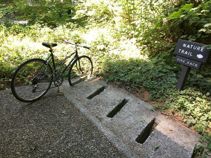 Bike securely locked in a concrete bike rack along a nature trail surrounded by greenery and sunlight.