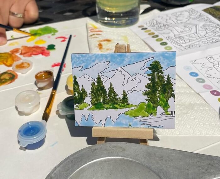 Miniature landscape painting in progress with paints and brushes on table, a dopamine hit from creative novelty finds.