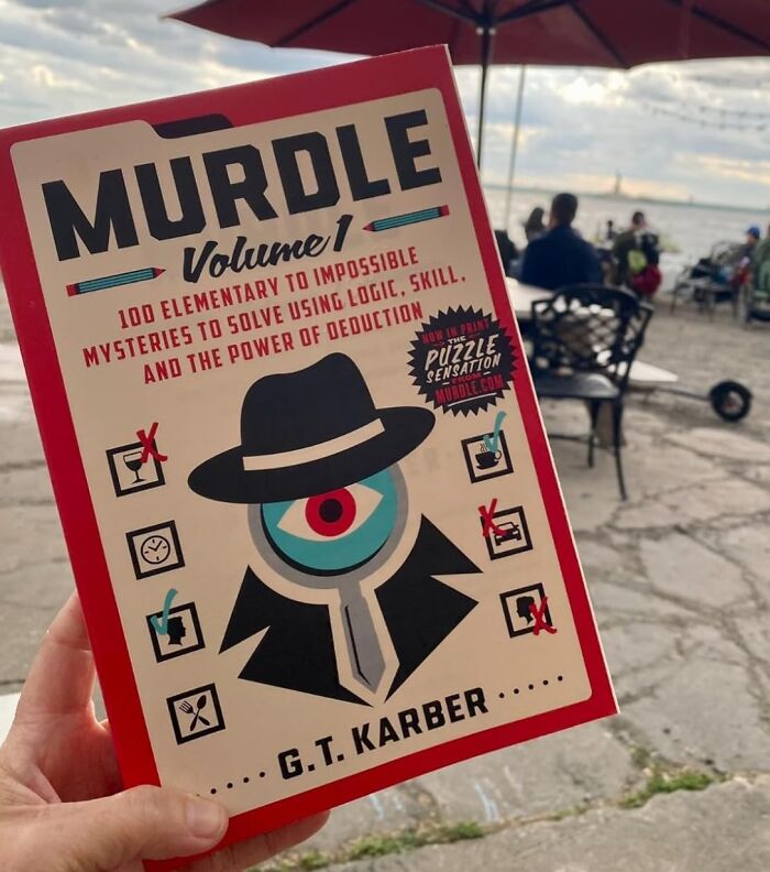 Hand holding MURDLE puzzle book by G.T. Karber, a novelty find for a dopamine hit with logic and deduction challenges.