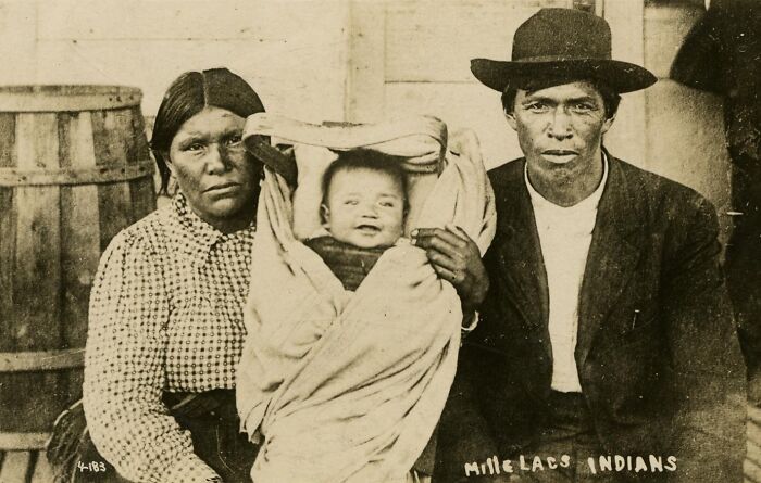 Vintage Native American family photo showing parents with a swaddled baby in traditional and early 20th century clothing.