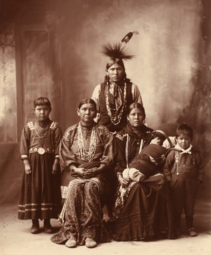 Vintage Native American family photo featuring traditional clothing and accessories in a sepia-toned portrait setting.