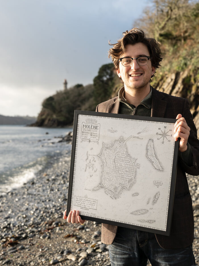 Young man holding a vintage map of an island by the rocky shore, highlighting fascinating world geography features.