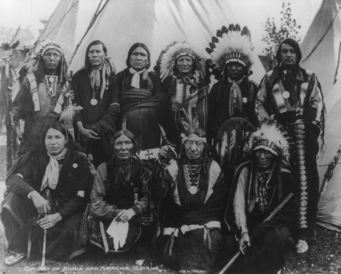 Vintage Native American family group photo featuring traditional clothing and headdresses in a historical outdoor setting.
