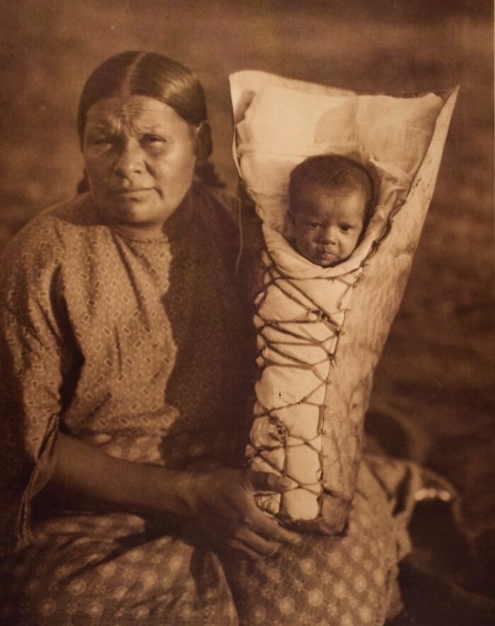 Vintage Native American family photo showing a woman holding a baby wrapped in a traditional cradleboard.