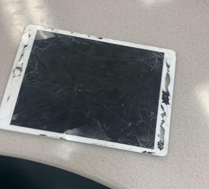 Damaged tablet with a severely c*****d screen on a desk, illustrating that not all schools are created equal.