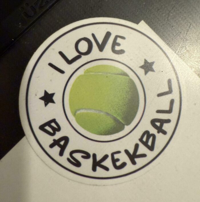 Sticker with a misspelled basketball phrase showing a tennis ball, highlighting unusual school moments and school differences.