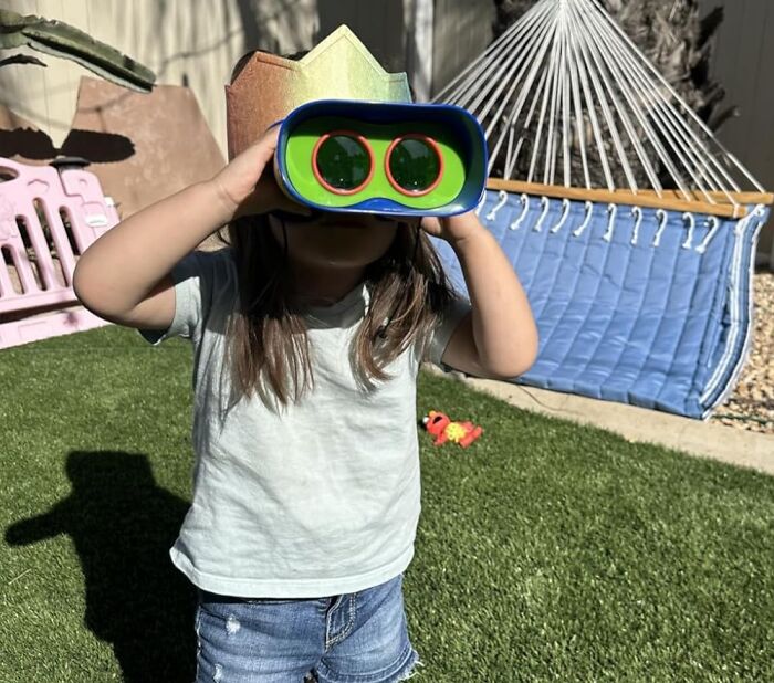 Child playing outdoors with colorful binocular toy, wearing a crown, illustrating fun toys under 20 dollars gift ideas.