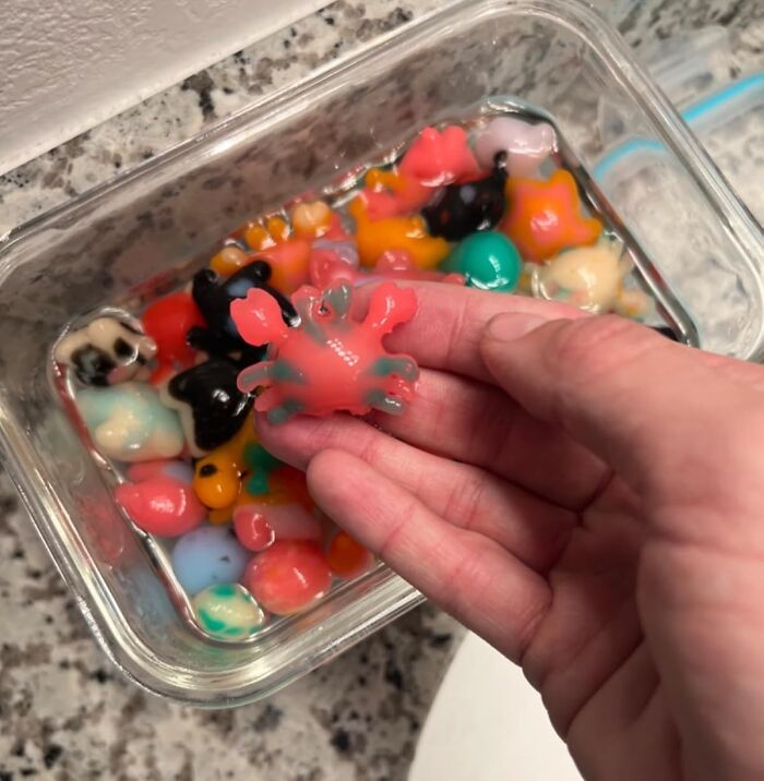 Colorful small toys under 20 dollars in water, with a hand holding a red crab-shaped toy for gifting ideas.