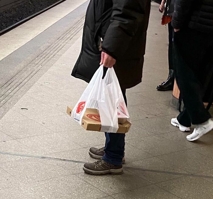 Person holding a plastic bag carrying a pizza box, demonstrating a genius solution to an everyday carrying problem.