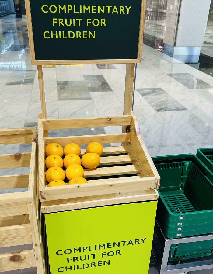Wooden crate with complimentary fruit for children featuring bright oranges in a public space solving overlooked snack needs.