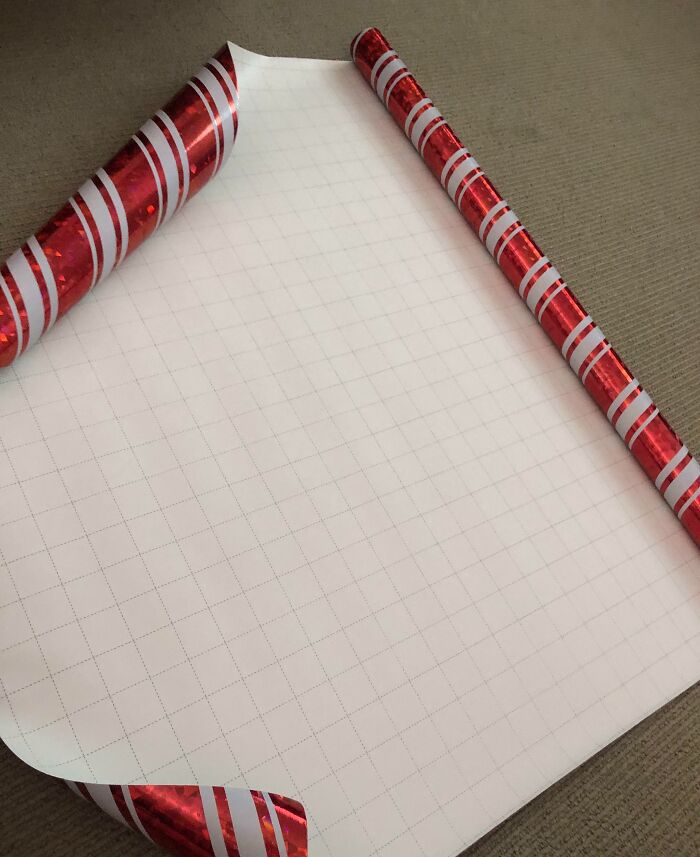 Glossy red and white striped adhesive paper partially peeled back, showcasing a grid pattern underneath on a brown surface.