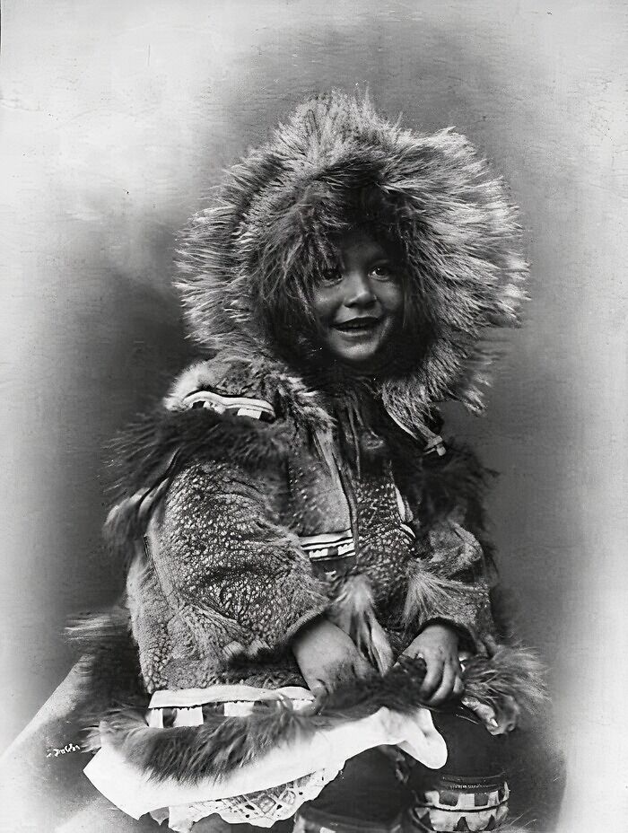 Inuit child wearing traditional fur parka smiling in a historic black and white photo showcasing Inuit spirit and culture.
