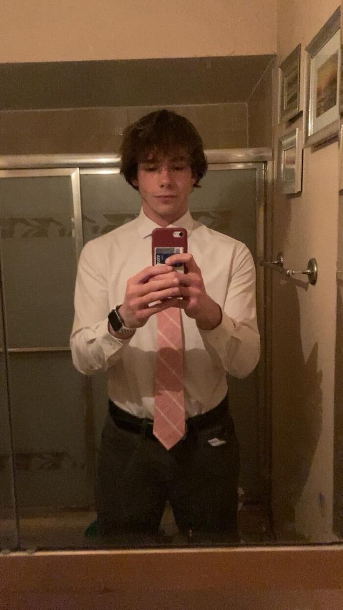 Young man wearing a white shirt and pink tie taking a selfie in a bathroom mirror, reflecting the beauty of planet earth.
