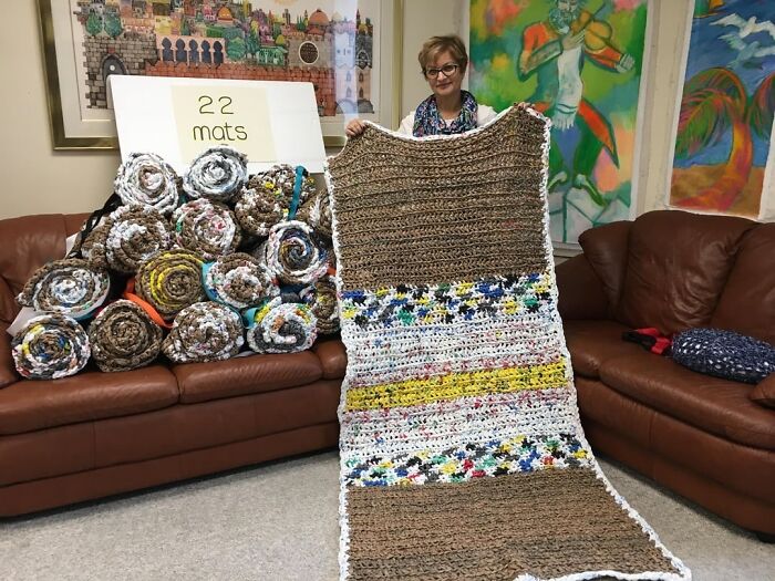Woman holding a handmade woven mat with 22 rolled mats on a couch, showcasing the beauty of planet Earth crafts.