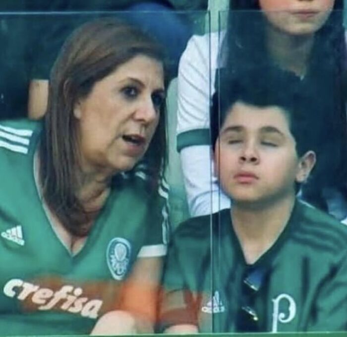 Woman and boy in green sports jerseys sitting behind a glass panel, capturing a candid moment of the beauty of planet earth.