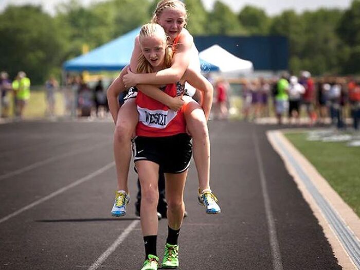 Two young athletes on a track, with one giving a piggyback ride, showcasing teamwork and the beauty of planet Earth.