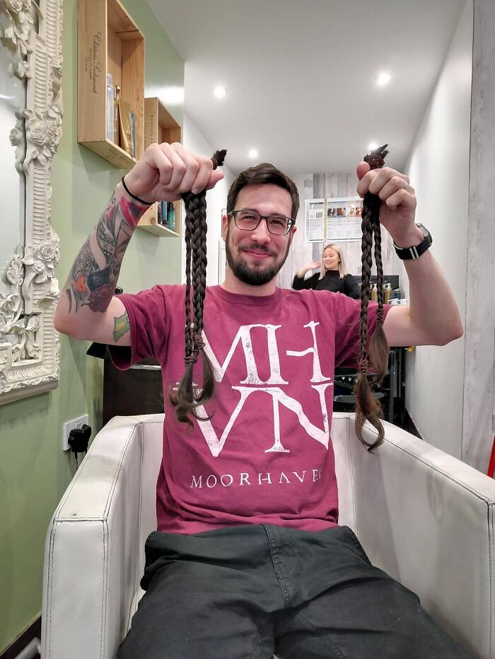 Man with tattoos holding two long braided hair strands in a salon, showcasing beauty of planet earth through natural hair.