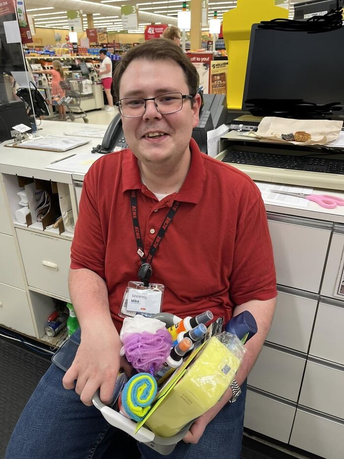 Man wearing glasses and a red shirt sitting at a store counter holding assorted cleaning products representing care for the planet Earth.