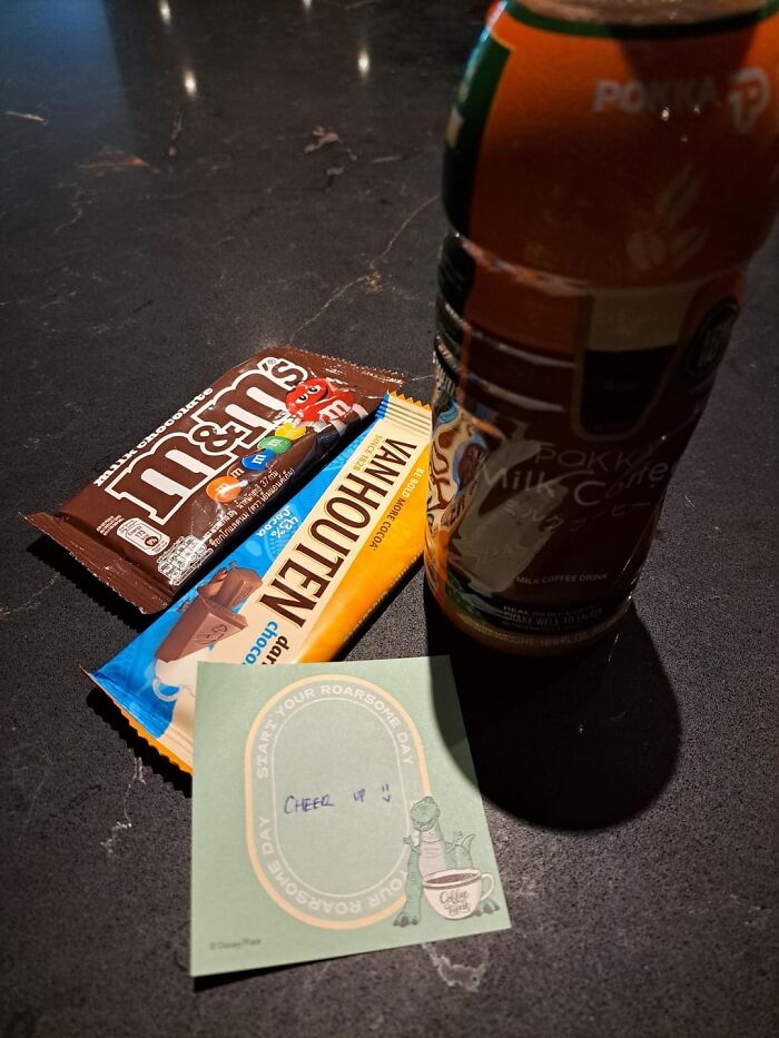 M&Ms and Van Houten chocolate bars beside a milk coffee drink and a cheerful note on a dark marble surface.