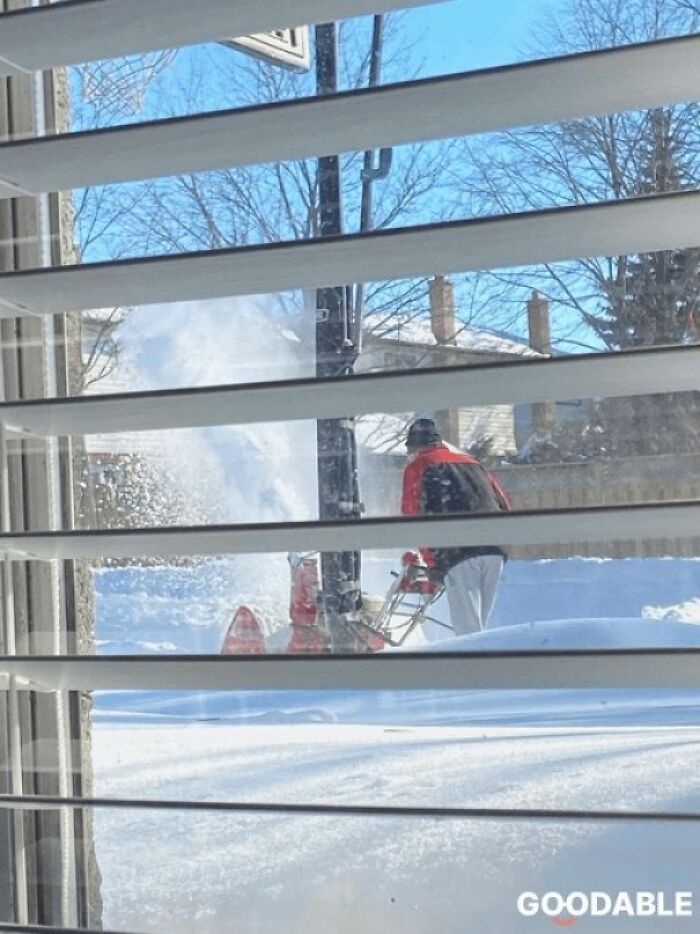 Person clearing snow outside window blinds on a sunny winter day, showcasing beauty of planet earth in snowfall.