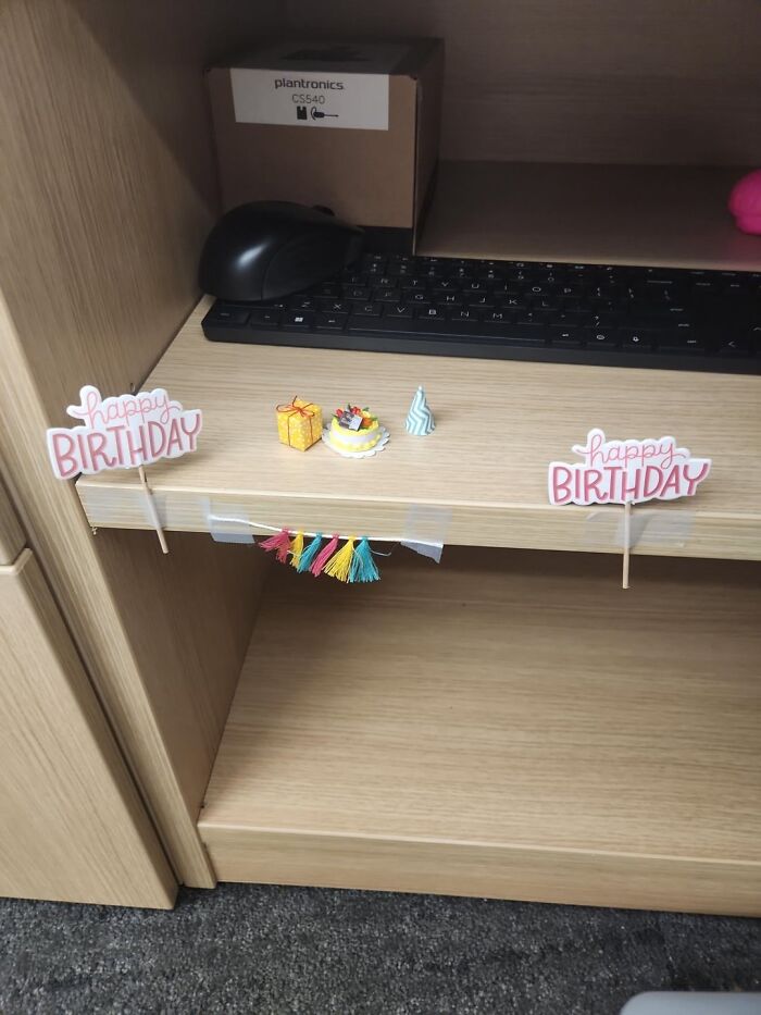 Miniature birthday decorations on a wooden desk shelf near a keyboard and computer mouse, showcasing the beauty of planet earth.