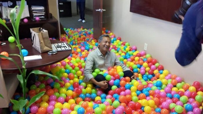 Man sitting and smiling in an office filled with colorful plastic balls showing the beauty of planet earth theme.