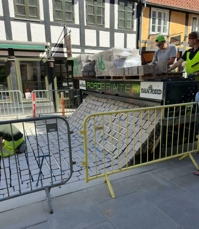 Street workers using a road printer machine to lay bricks, showcasing a genius solution to overlooked construction problems.