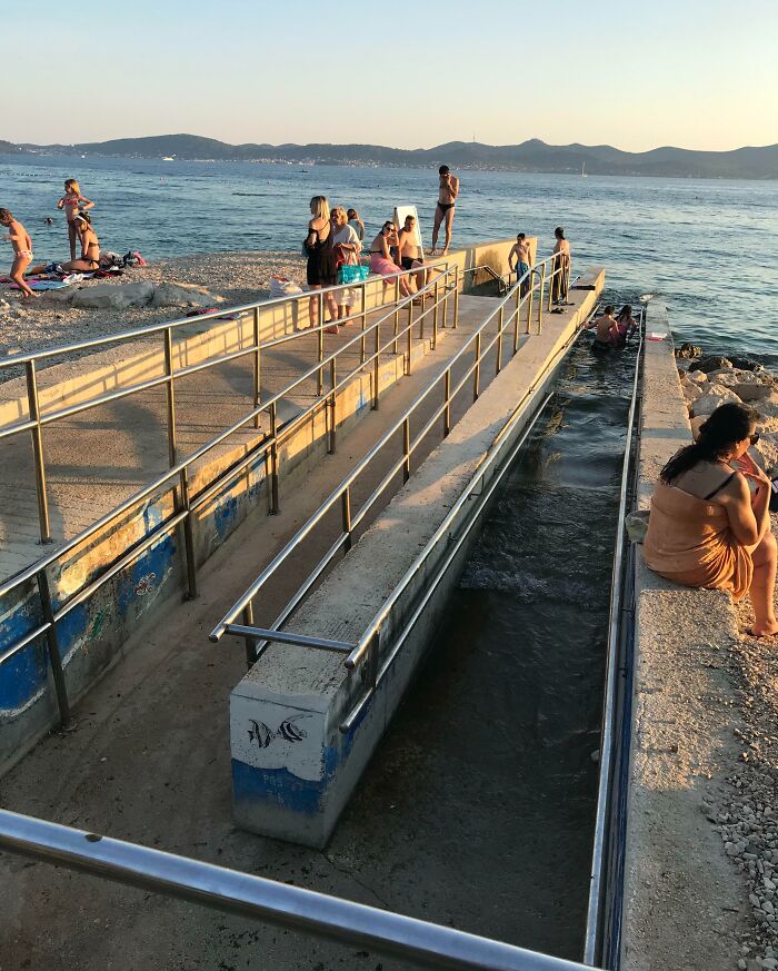 Beach with people enjoying the ocean near a concrete ramp with metal railings, showcasing genius solutions to overlooked problems.