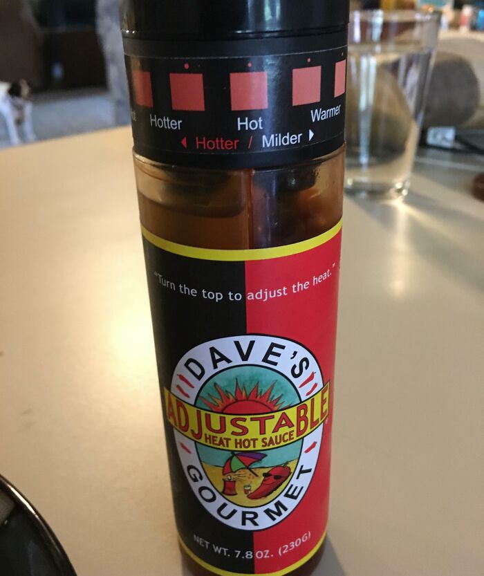 Bottle of Dave's Adjustable Heat hot sauce with labeled heat settings from milder to hotter on a kitchen table.
