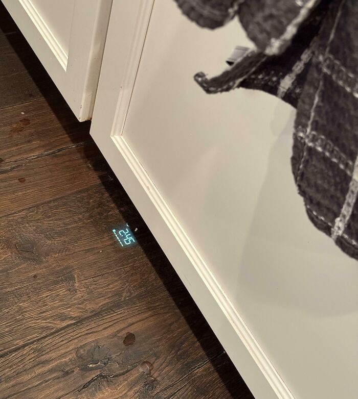 Digital clock projecting time onto wooden floor beneath white kitchen cabinets, showcasing a genius solution to overlooked problems.