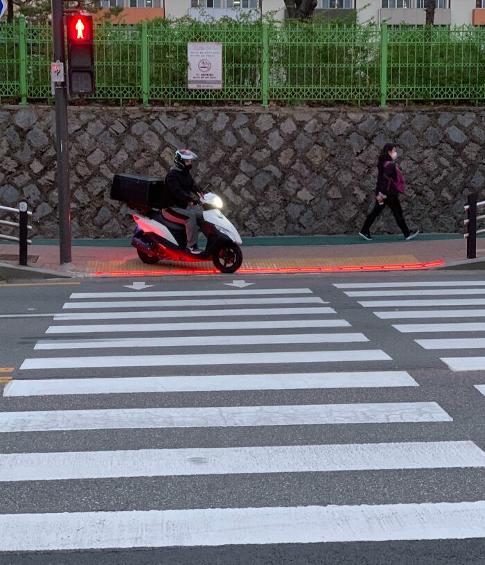 Motorcycle stopped at red light with pedestrian crossing and sidewalk safety innovation in urban setting.