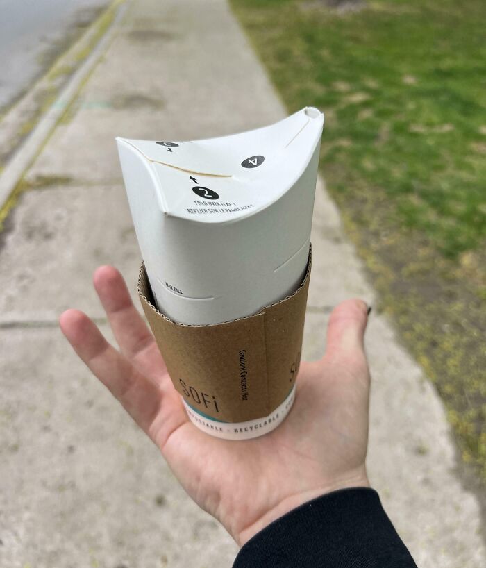 Hand holding a foldable paper cup with a cardboard sleeve, showcasing a genius solution to an overlooked problem outdoors.