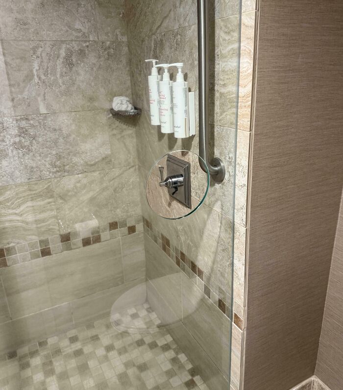 Bathroom shower with wall-mounted soap dispensers and a small adjustable mirror showcasing genius solutions