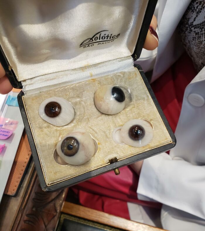Box containing four realistic prosthetic eyes displayed by person in white coat, a captivating medical photo with disturbing elements.