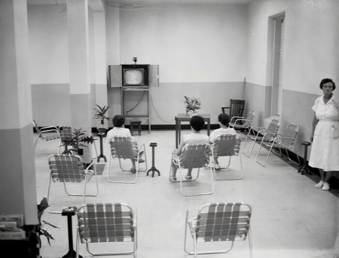 Black and white photo of people seated in a sparse room watching TV, showing everyday life in 1950s Florida.