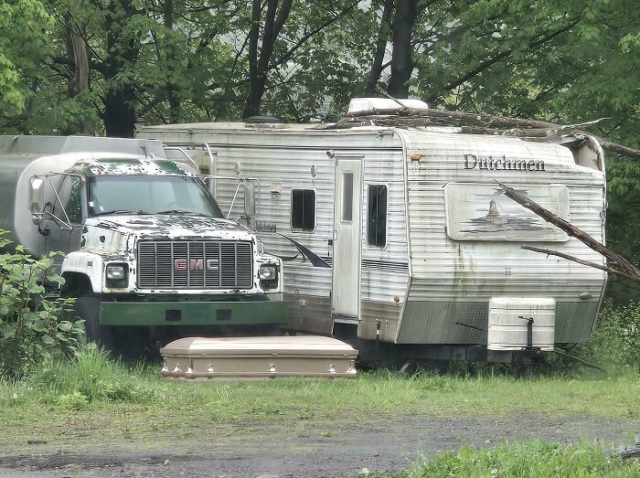 Old camper and truck parked in the woods near fallen branches, evoking neighbor tales that might make you want to move to the woods.