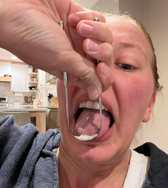 Person using a metal tongue scraper to improve oral hygiene, demonstrating a low-effort product for high-anxiety body issues.