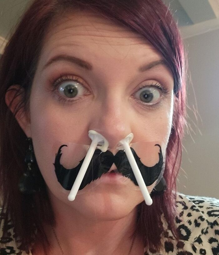 Woman using low-effort product with nose clips and fake mustache to tackle high-anxiety body issues in a humorous way.