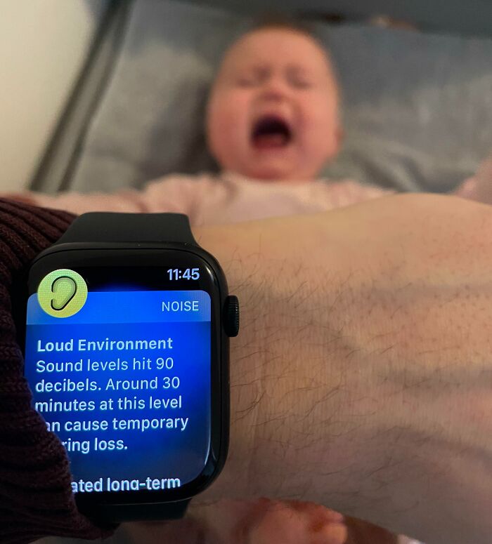 Smartwatch displaying loud noise warning on a dad's wrist with a crying baby in the background, hilarious dads nailing fatherhood.