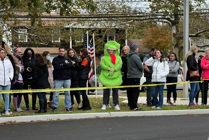 Man dressed as a dinosaur standing among a crowd behind caution tape, showcasing hilarious dads nailing fatherhood moments.