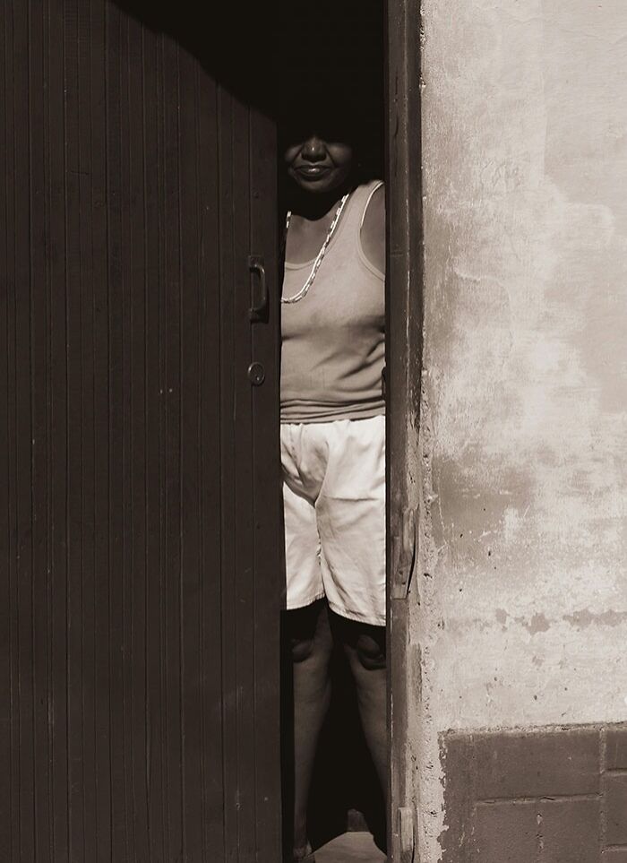 Person standing partially hidden behind a door, evoking neighbor tales and the mystery of moving to the woods.