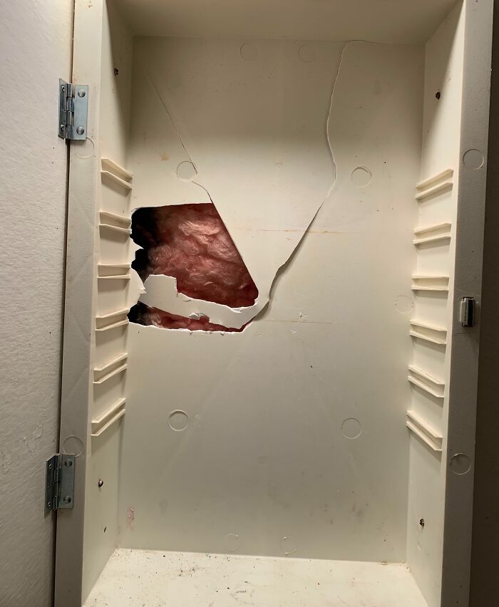 Empty cabinet with a large hole damaged drywall behind it, related to neighbor tales in a wooded area move context.