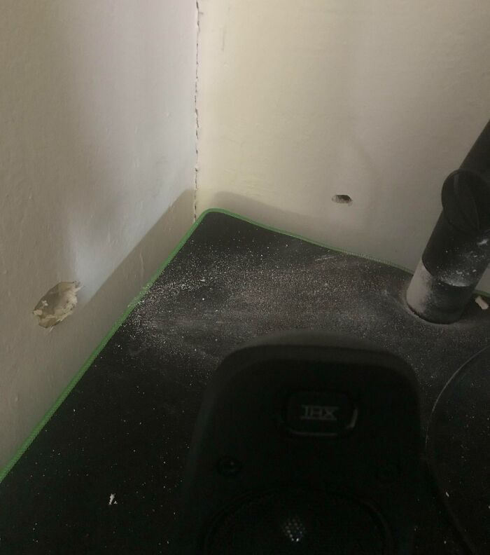 Corner of a room with holes in the wall and dust on a black surface, illustrating neighbor tales in a wooded setting.