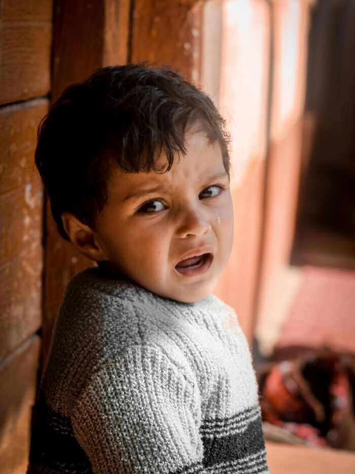 Young boy crying inside a wooden cabin, capturing emotions in a peaceful woods setting for neighbor tales and nature stories.