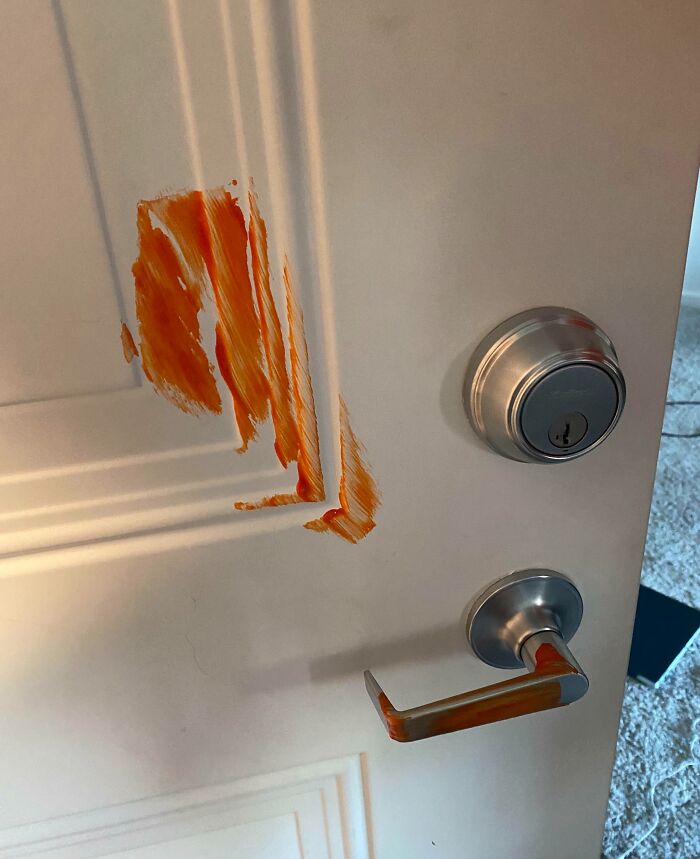 Close-up of a door with red paint smeared near handle and lock, showing unusual neighbor tales in a residential setting.