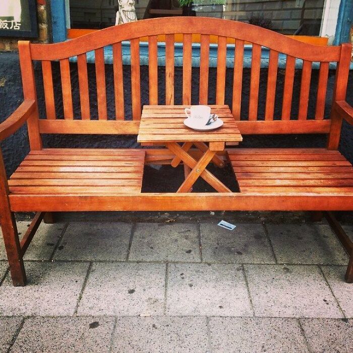 Wooden bench with built-in small table holding a coffee cup, showcasing small but genius things some countries do.