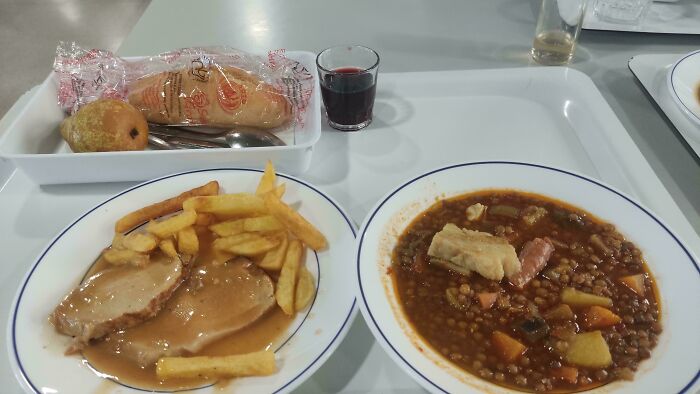 Tray with lentil stew, meat with fries, bread, and a small drink showcasing small genius things some countries do.