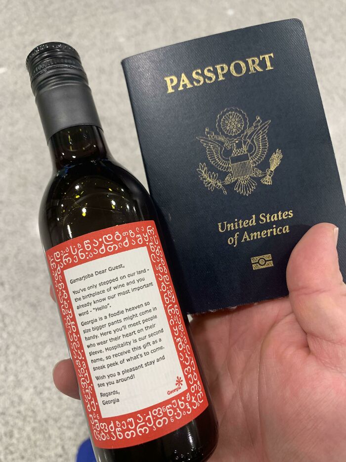 Hand holding a small wine bottle with a welcome message and a US passport, showcasing small genius things some countries do.